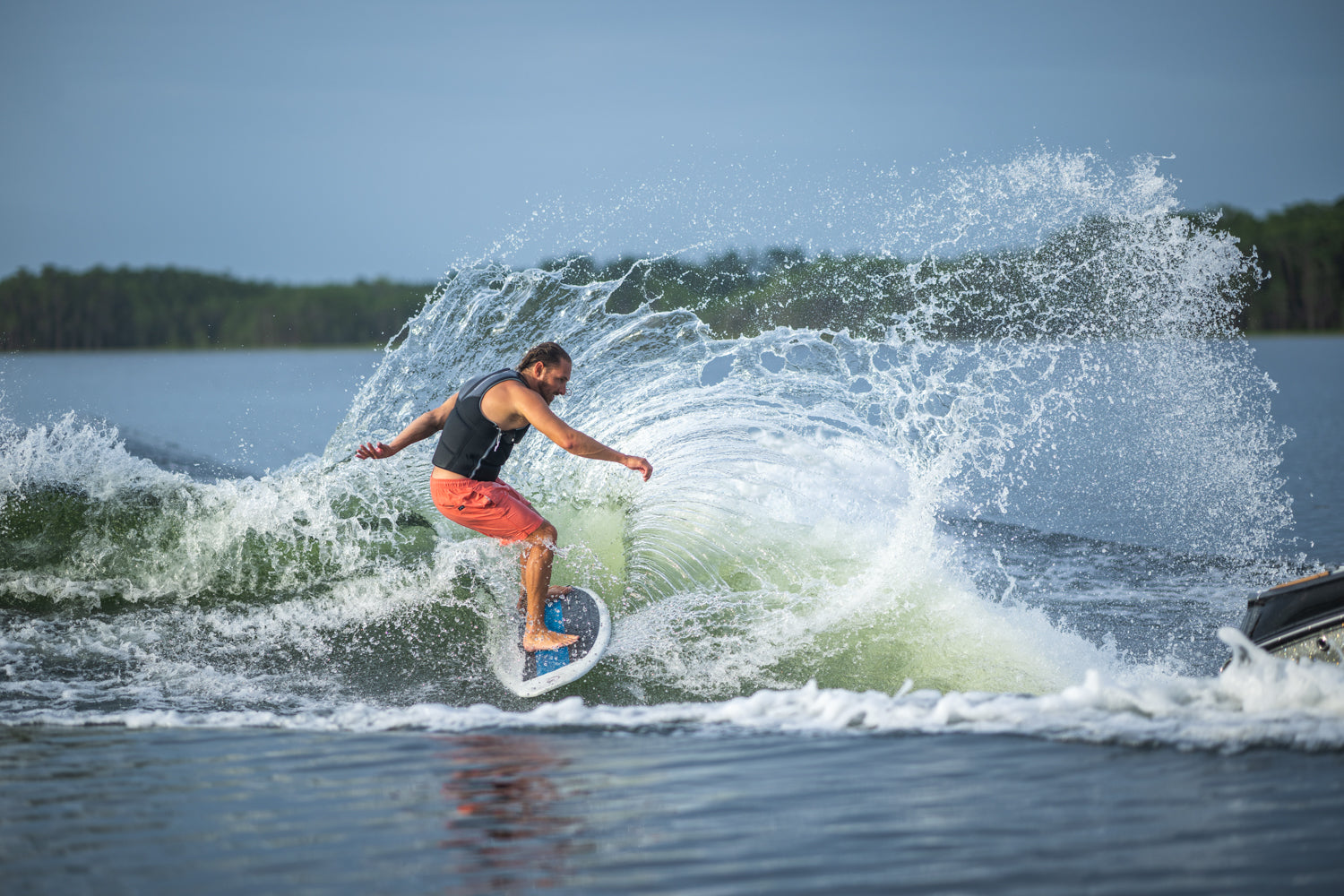Person wakesurfing on a lake with a large wave splash behind.