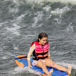 Young girl on kneeboard, wearing a pink life jacket, gliding over water with Wild Thing.