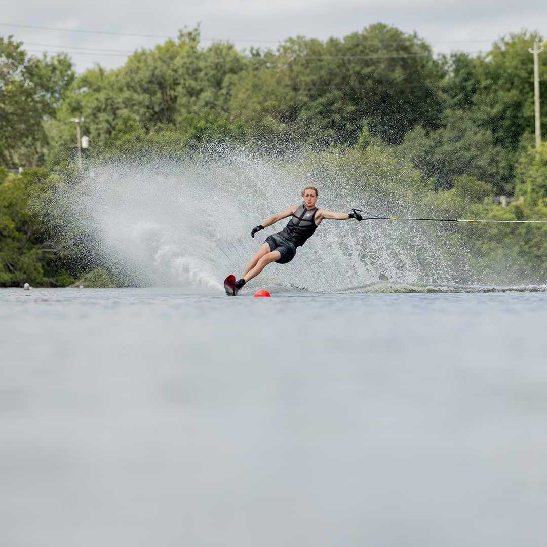 A water skier carving through a slalom course on a 2024 Carbon V ski, creating a powerful spray behind them.