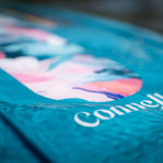 Close-up of the Lotus wakeboard’s surface, showing a blue and pink marbled graphic with the Connelly logo in water.