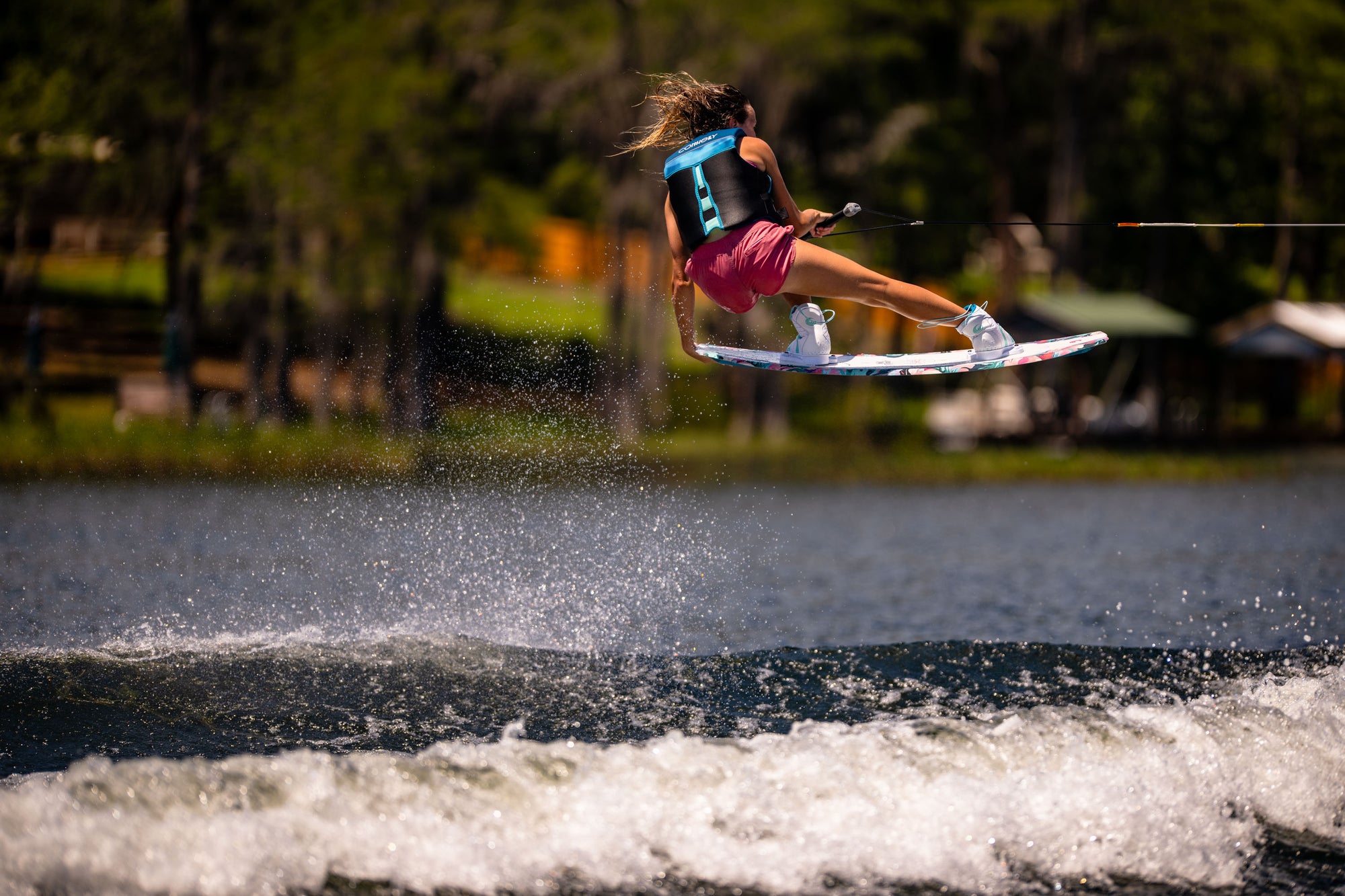 Person wakeboarding and performing a jump over water with trees in the background.