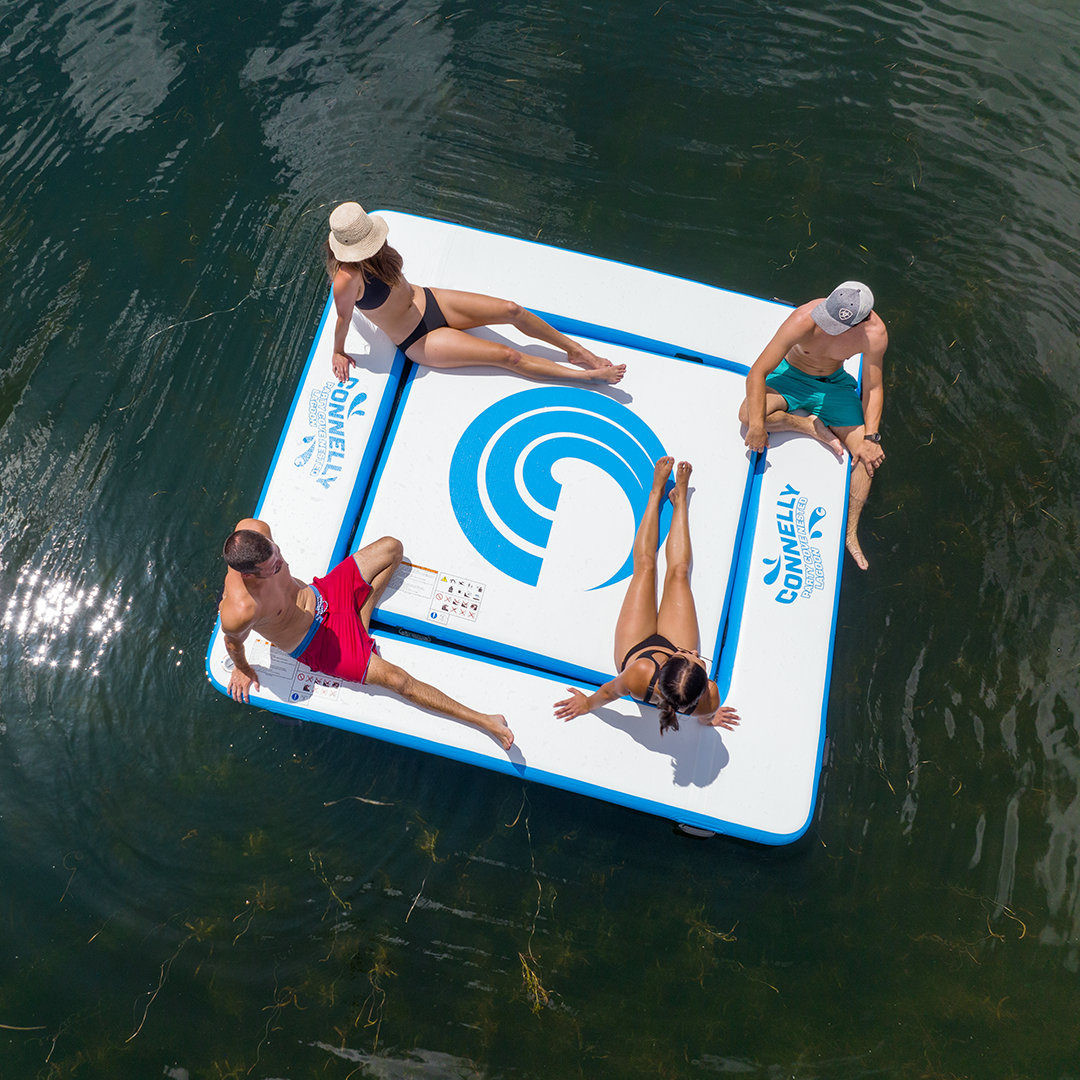 Four people relaxing on a floating platform in water, viewed from above.