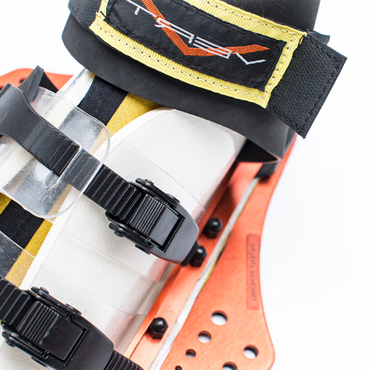Close-up of a ski boot with black buckles and an orange baseplate.