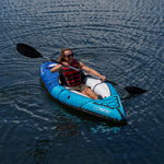 A man in a red life jacket paddles the Nautic 9.5 inflatable kayak on a calm lake.
