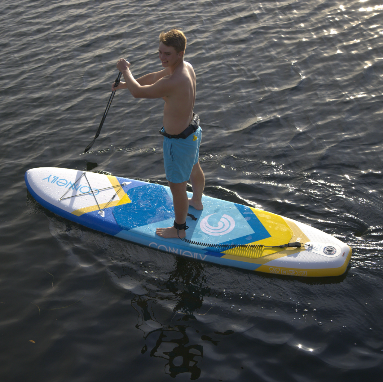 Side view of a man using the Tahoe ISUP, showing the paddleboard’s blue, yellow, and white design.