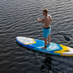 Man paddling the Tahoe ISUP on the water, wearing blue shorts and a waist leash.