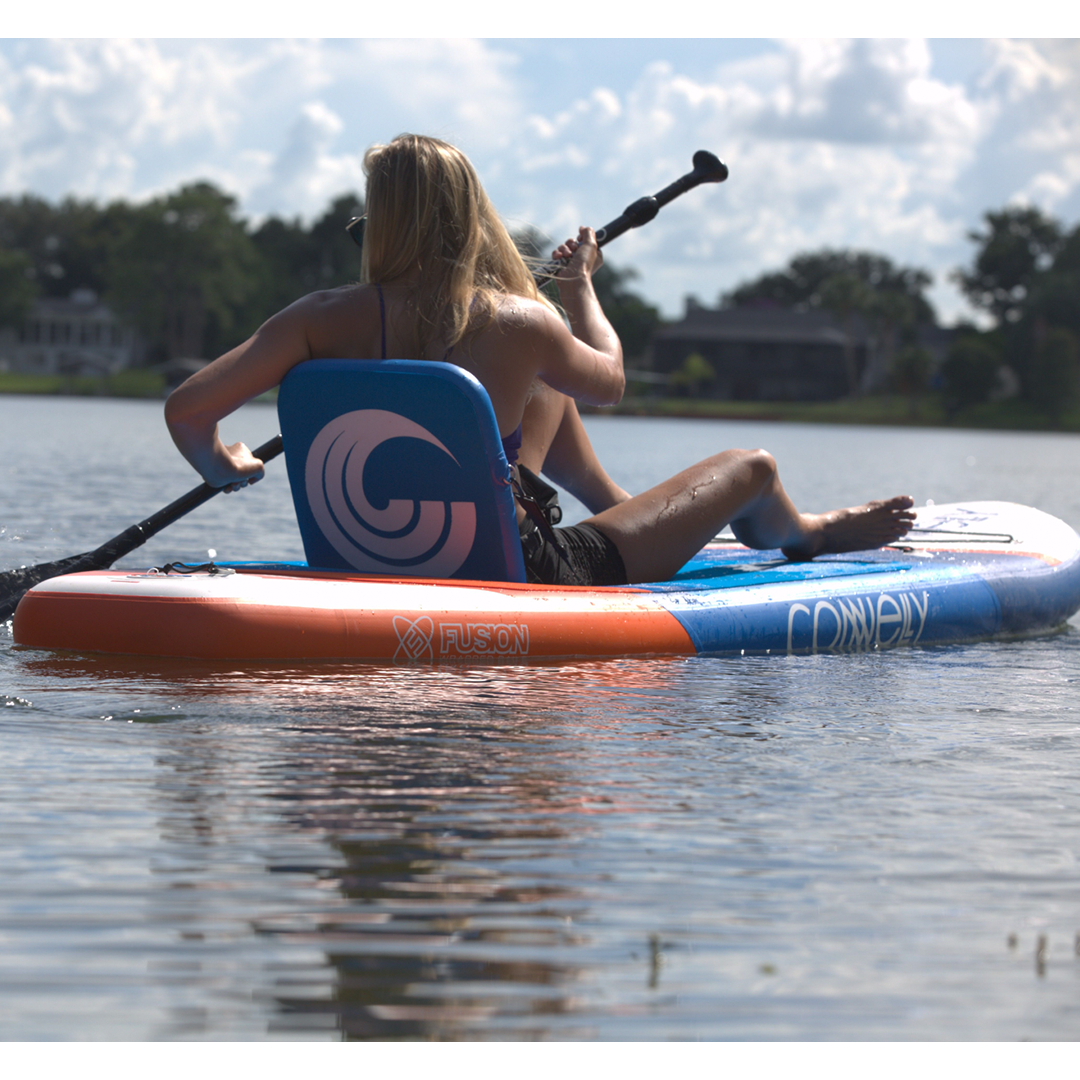 A woman paddles on the Pacific ISUP in a seated position, using the attached backrest for support.