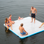 Side view of the Party Cove Dock Deluxe with people sitting and standing on its light woodgrain surface and blue border.