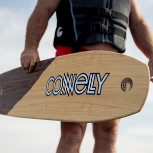 A skier holding the Connelly Big Easy ski with a bold logo on the woodgrain finish.