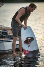 Lifestyle shot of a rider holding the PURE wakeboard with attached bindings while standing in shallow water.