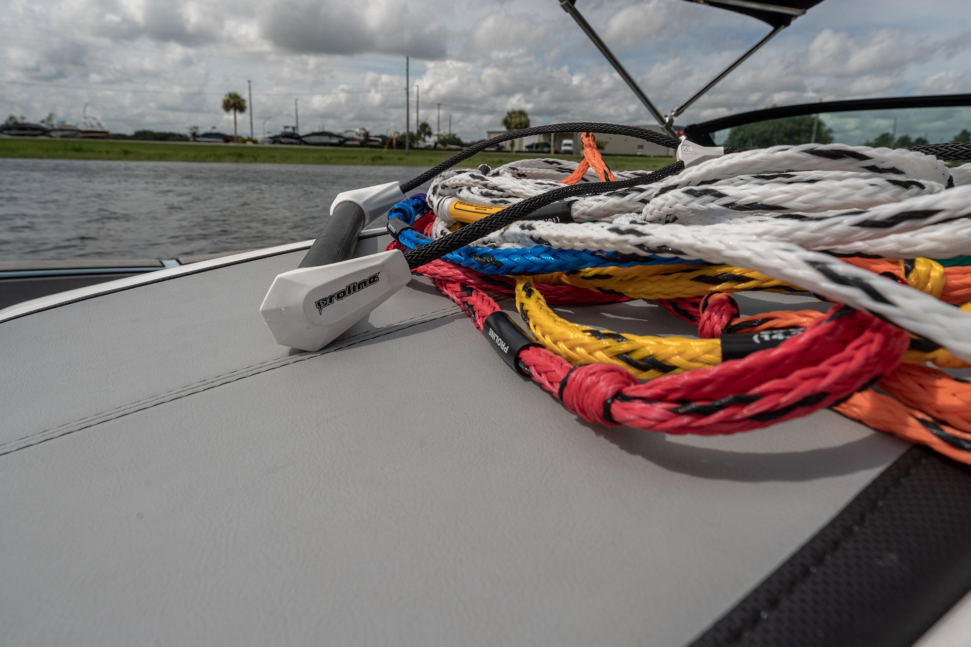Colorful tow ropes and a white handle piled on a boat gunwale beside a lake.