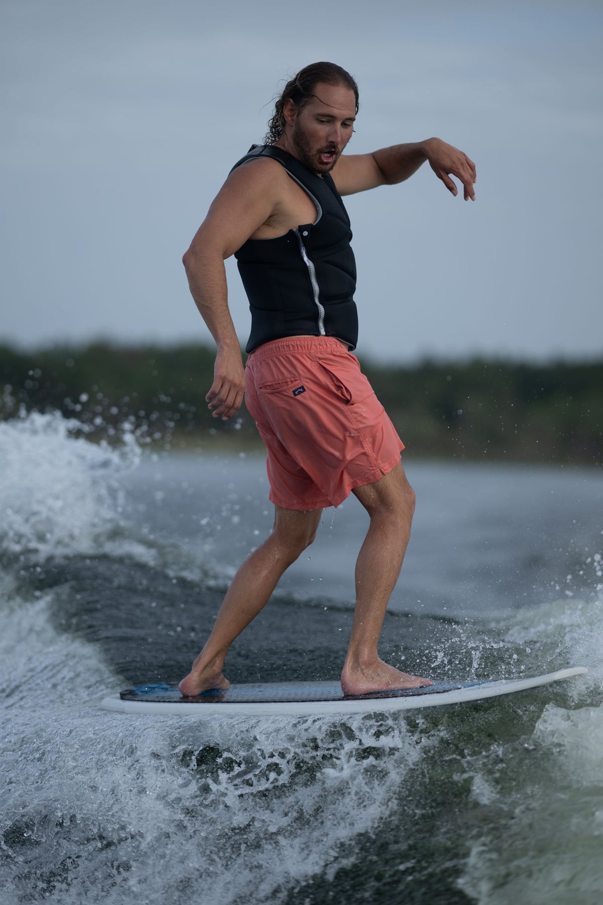 A male rider shifts his weight back on the Bentley board while wakesurfing, maintaining balance on the wave.
