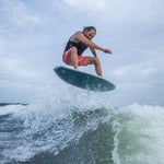 A male wakesurfer catches air on the Bentley board, lifting above the wave with water spray surrounding him.