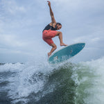 A male rider carves through a wake on the Bentley wakesurf board, maintaining balance with water splashing around him.