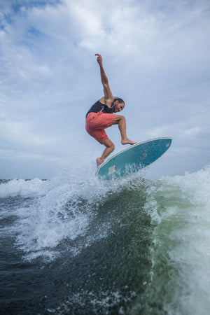 A male rider carves through a wake on the Bentley wakesurf board, maintaining balance with water splashing around him.