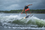 A male wakesurfer launches off a wake on the Benz board, fully airborne with water spray beneath him.