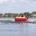 Three riders kneeling on the Big Easy 3 tube while being pulled across the water, gripping the front handles for stability.