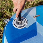 Close-up of a hand inflating the Stash iSUP, with the Connelly valve and blue geometric pattern.