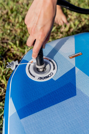 Close-up of a hand inflating the Stash iSUP, with the Connelly valve and blue geometric pattern.