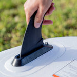 Close-up of a hand installing the removable fin on the Stash iSUP, with a white textured base.