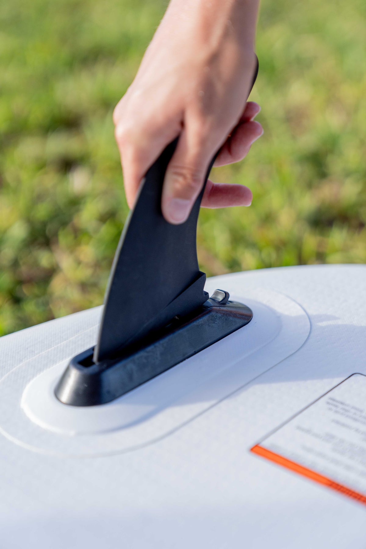 Close-up of a hand installing the removable fin on the Stash iSUP, with a white textured base.