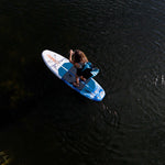Overhead view of a woman paddling on the Stash iSUP in dark water, carrying the backpack.