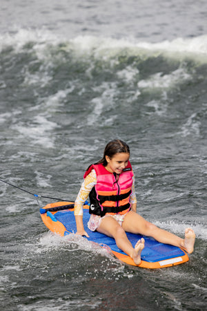 Young girl on kneeboard, wearing a pink life jacket, gliding over water with Wild Thing.
