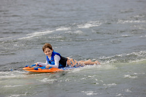 Child smiling on a Wild Thing orange kneeboard with handles, wearing a life vest.