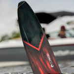 The 2024 Carbon V ski partially submerged, showcasing its deep red top sheet with a bold black V-shaped accent.