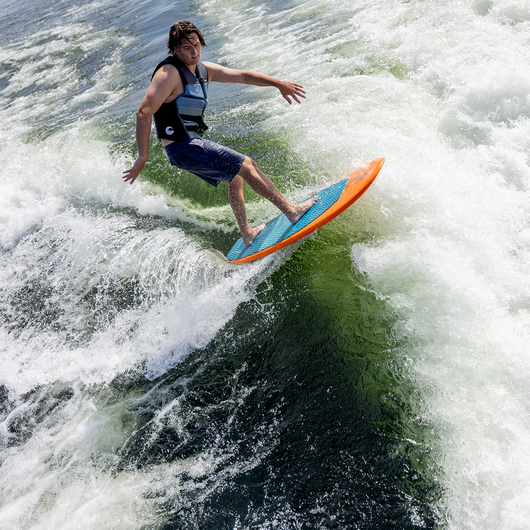 Man wearing a life vest wakesurfing on the Cloud 9 board, balancing on a wave with a relaxed stance.