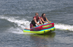 Front view of the Fun 2 towable tube with two riders kneeling, gripping handles, and skimming across the water.
