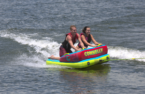 Front view of the Fun 2 towable tube with two riders kneeling, gripping handles, and skimming across the water.