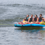 Fun 4 towable tube with four riders gripping handles and gliding across the water behind a boat.