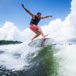 A rider catching air on the HABIT Skim wakesurf board, launching above the wave with arms outstretched.