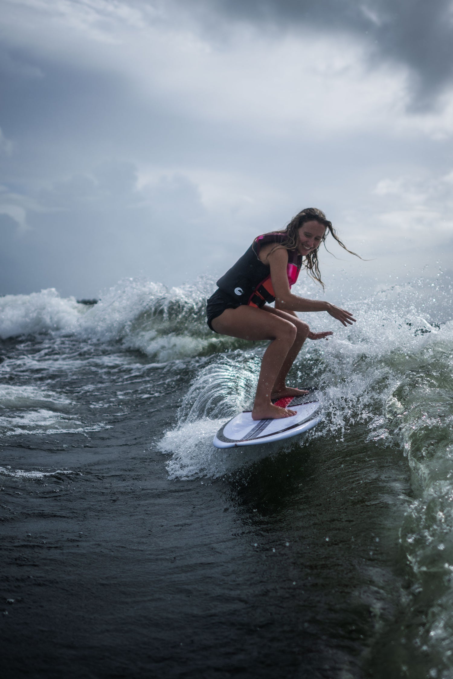 A surfer riding the Jet wakesurf board on a wave, wearing a life vest and balancing with a happy expression.
