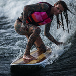 A woman crouches while riding the Lil Easy wakesurf board on a wave, showing control and balance.