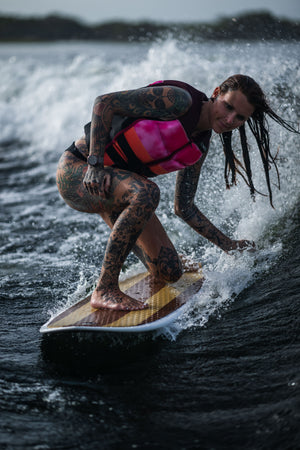 A woman crouches while riding the Lil Easy wakesurf board on a wave, showing control and balance.