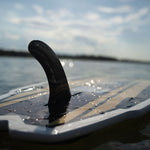 Close-up of the Lil Easy wakesurf board floating on the water, showing the black fin and woodgrain deck design.