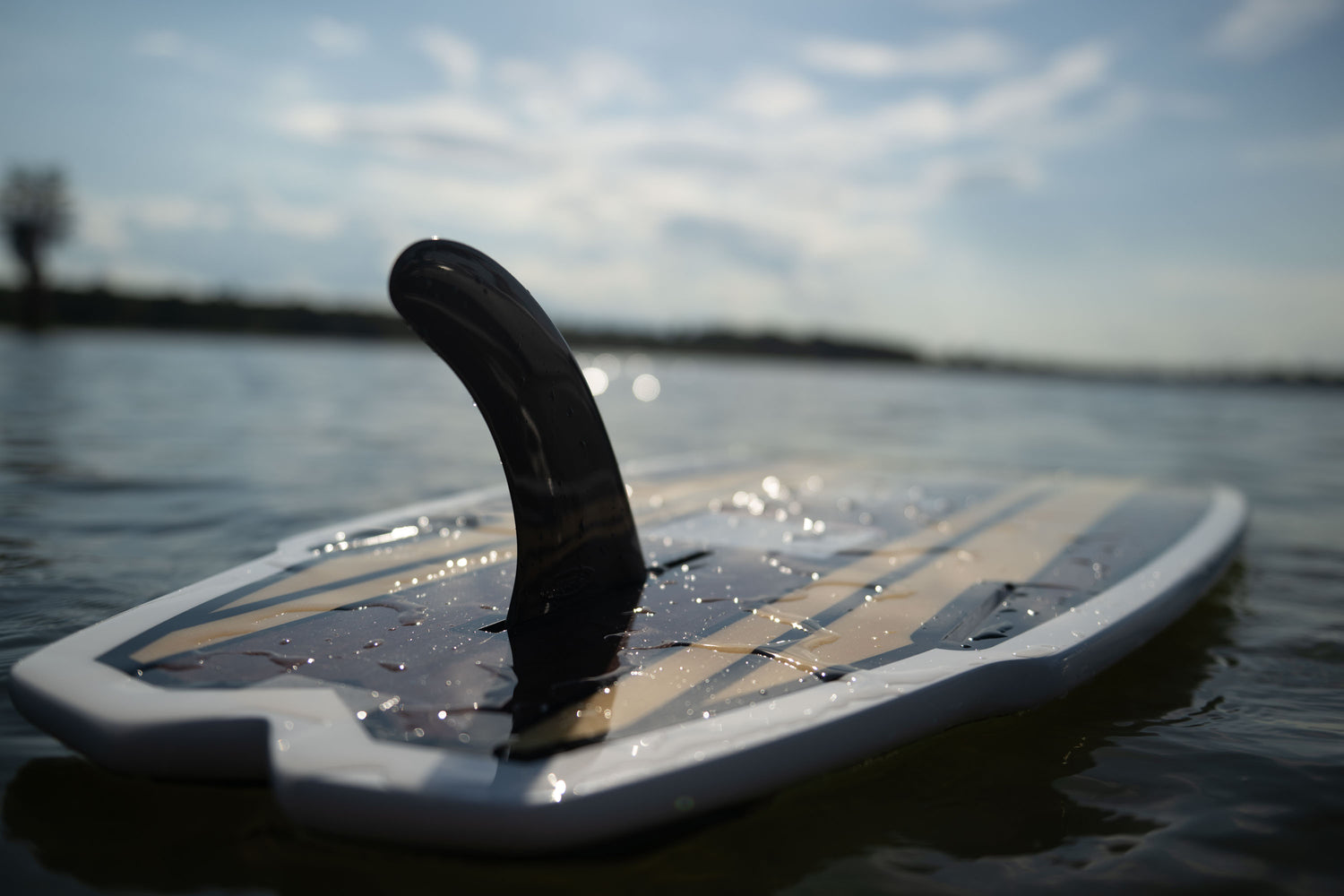 Close-up of the Lil Easy wakesurf board floating on the water, showing the black fin and woodgrain deck design.