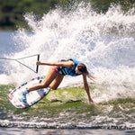 Wakeboarder carving a wave on the Lotus wakeboard, leaning into the water with one hand while creating a large splash.