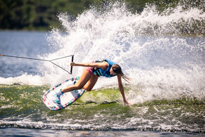 Wakeboarder carving a wave on the Lotus wakeboard, leaning into the water with one hand while creating a large splash.