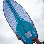 A person holds the Ono wakesurf board, showcasing its blue and white geometric traction pad and fin slots.
