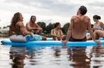 Low-angle view of six people on the Party Cove Lagoon Deluxe, highlighting its sturdy inflatable frame and social seating.