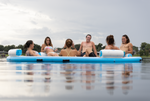 Side view of the Party Cove Lagoon Deluxe on water with six people, showing its blue and white ring and padded armrests.