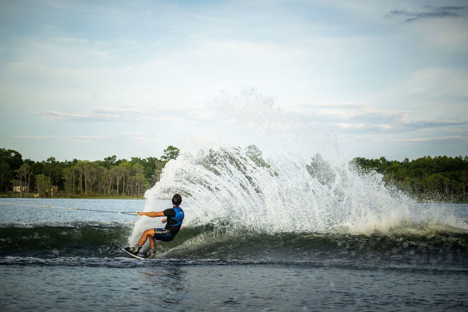 Rider carving a powerful turn on a Blaze wakeboard, creating a dramatic spray of water behind them.