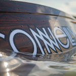 Close-up of the Connelly Big Easy wakeboard floating on the water, with droplets highlighting its sleek woodgrain design.