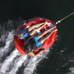 Aerial view of two people riding the Racer 2 towable tube, gripping handles as they glide over the water.
