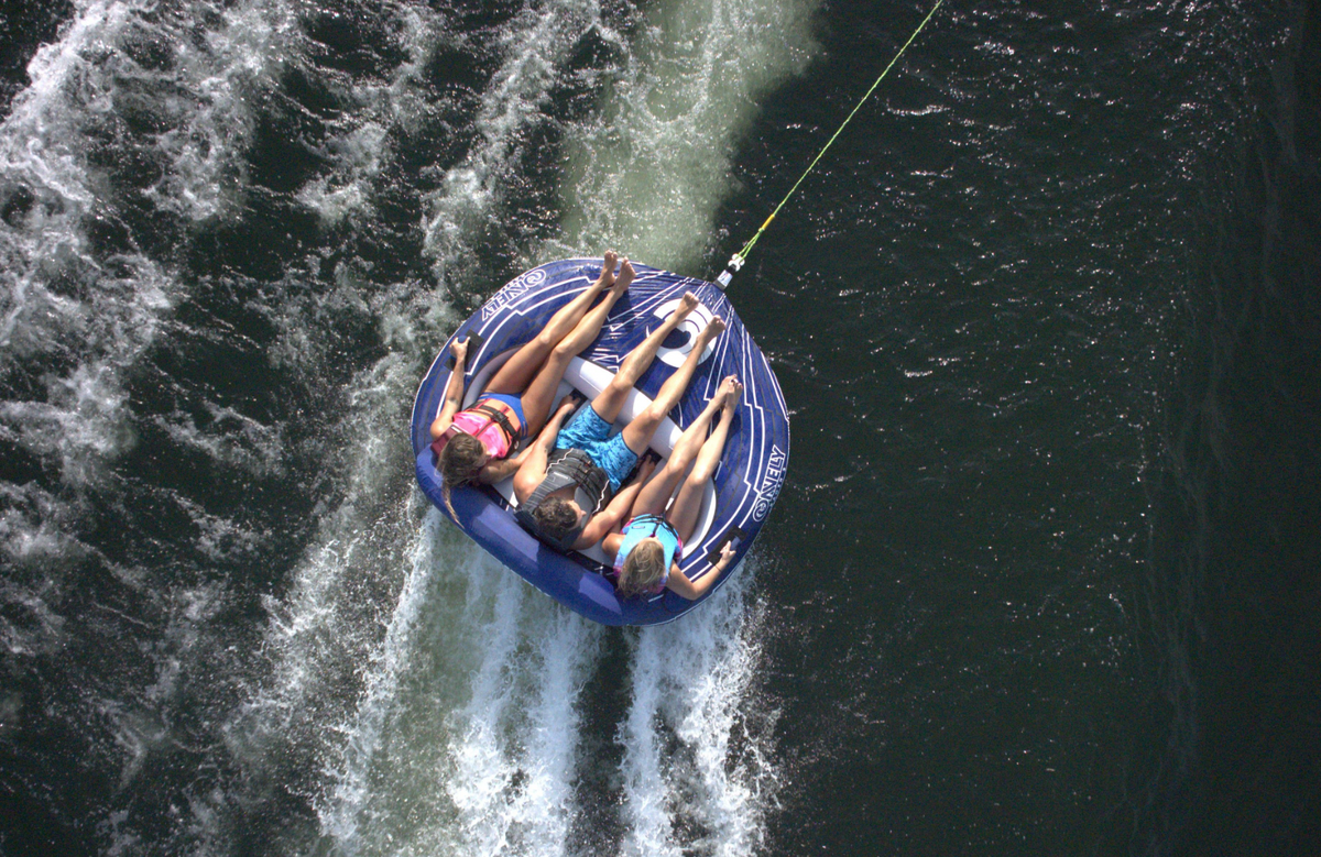 Aerial view of three riders on the Racer 3 towable tube, gripping handles as they skim the water.