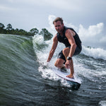 A male surfer in a black life vest carves through a wave while riding the Seer wakesurf board.