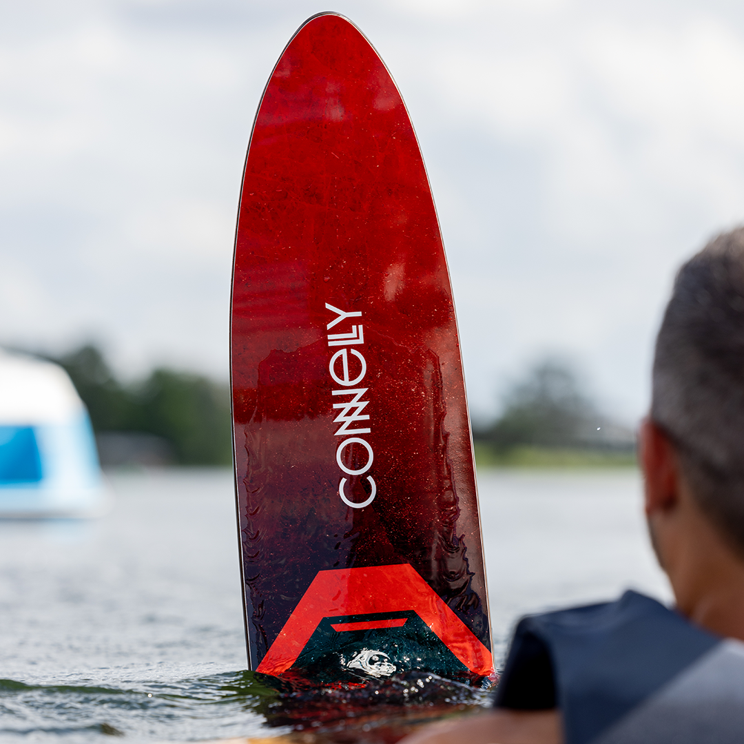 Close-up of the Shortline ski tip emerging from the water, featuring a red glossy finish with the Connelly logo in white.